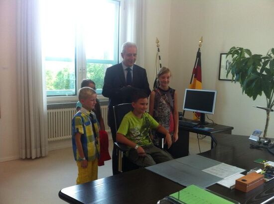 Minis&shy;ter&shy;prä&shy;si&shy;dent räumt seinen Stuhl für inter&shy;es&shy;sierte Gäste im Gläsernen Regie&shy;rungs&shy;viertel.