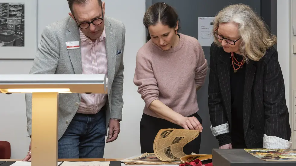 Thomas Stern (l., SLUB, Deutsches Archiv der Kulinarik) schaut mit Lilly Böhm und Maraike Wittbrodt (Mitte und rechts, Enkelin und Tochter von Ursula Winnington) auf ausgewählte Sammlungsstücke aus deren Nachlass.