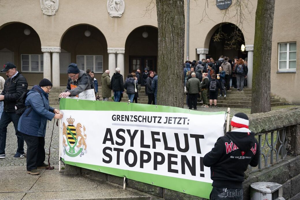 Teilnehmer einer Kundgebung der rechtsextremen Kleinstpartei Freie Sachsen halten vor dem Beruflichen Schulzentrum einen Banner mit der Aufschrift "Asylflut Stoppen"