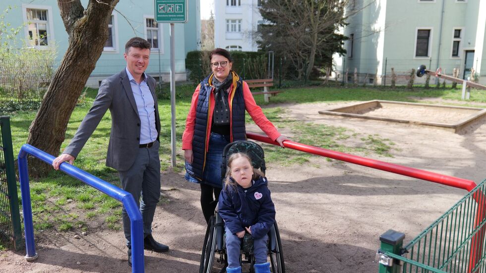 Bürgermeister Markus Renner (l.) und Kitaleiterin Carina Richter sind froh: Dank des erfolgreichen Projekts aus dem Bürgerhaushalt 2023 kann Ida (r.) nun den Spielplatz an der Bergstraße barrierefrei erreichen. 