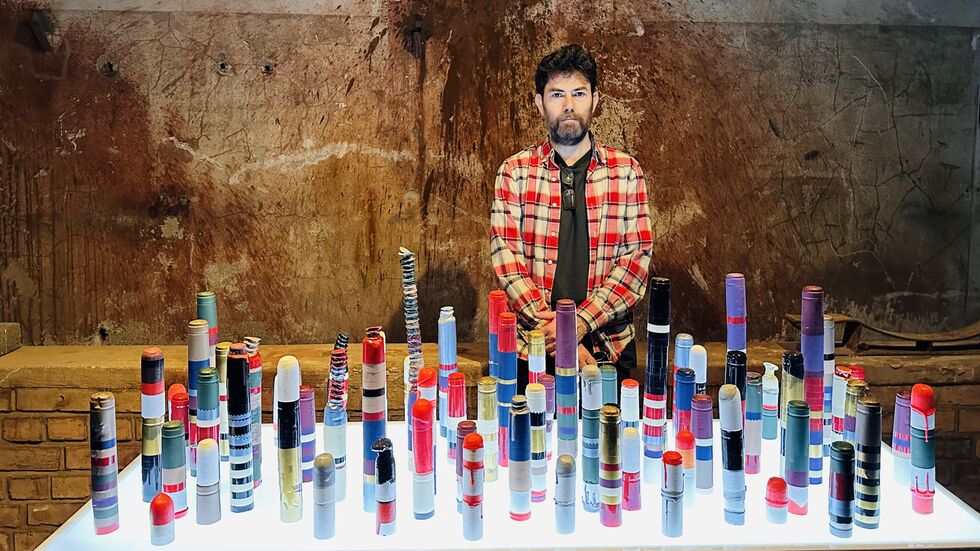 Der israelischen Künstlers Guy Goldstein vor seinen Kunstwerk von Türmen aus Verschlüssen von Weinflaschen