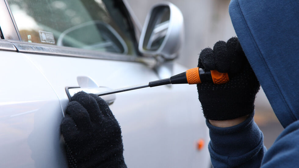Ein Dieb macht sich an einem Auto zu schaffen.