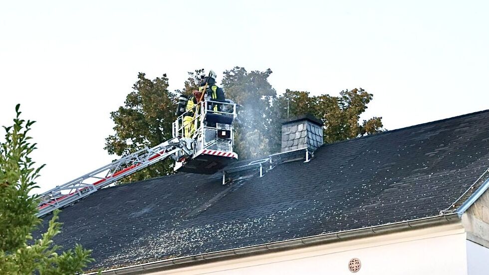 Rauch steigt aus dem Dach. Die Feuerwehr setzt eine Drehleiter ein